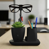 Black desk organizer holding glasses, plant, keys, and pens on a wooden desk.